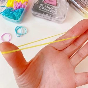 Close-up of highly elastic yellow hair band being stretched over a colorful assorted box