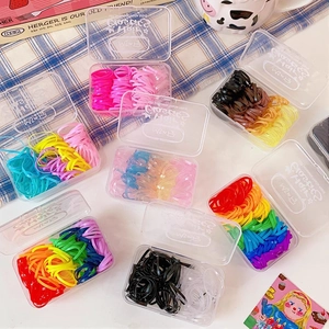 Close-up of jelly-colored elastic hair bands in clear storage cases on a plaid backdrop