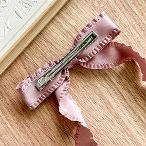 Detail of pink satin bow hair clip featuring pleated edges and silver metal duckbill clip