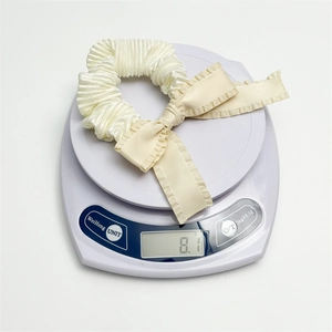Detail of a cream pleated bow hair scrunchie weighing 8.1g on a white scale