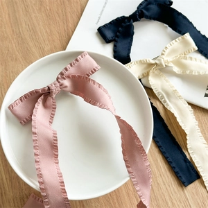Detail of satin bow hair clips with ruffled edges in pink, navy blue, and beige