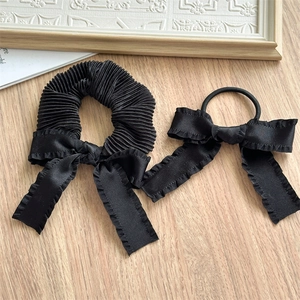 Detail of black pleated scrunchie and elastic hair tie with satin bow on wooden surface