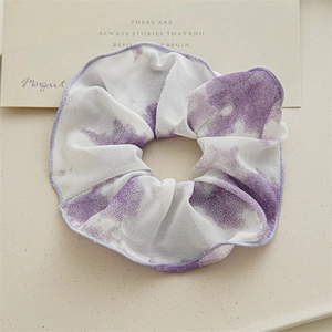 Détail d'un chouchou géant tie-dye violet et blanc posé sur un plateau élégant
