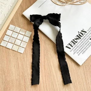 Detail of elegant black pleated fabric bow hair clip with long ribbons on a white magazine