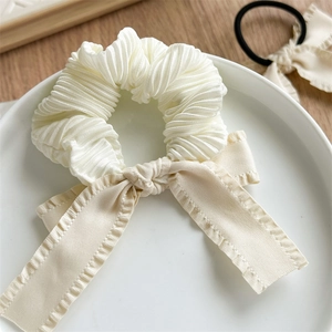 Detailed macro view of white pleated fabric hair scrunchie with silk cream bow decoration