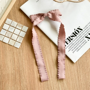 Close-up of pink pleated fabric bow hair clip with long ribbons on a stylist magazine background