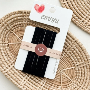 Close-up of black seamless elastic hair ties on a white card inside a woven tray