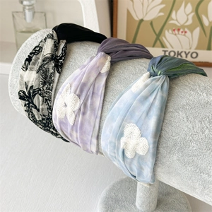 Three wide floral and tie-dye headbands with lace butterfly detail on a display stand