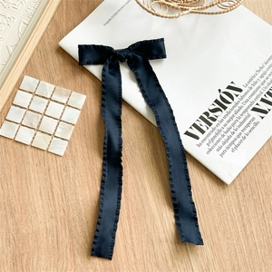 Detail view of black satin bow hair clip with ruffled edges on a magazine backdrop