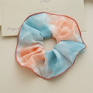 Détail d'un chouchou géant tie-dye avec dégradé bleu ciel et rose sur tissu texturé