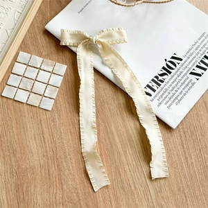 Detailed view of cream ruffled ribbon bow hair clip on a minimalist wooden background