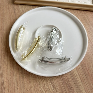Set of four gold and silver metal spring hair clips on a white ceramic plate