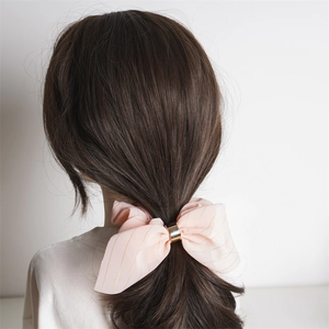 Détail d'un chouchou rose clair avec boucle dorée porté sur de longs cheveux bruns