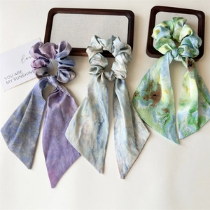 Close-up of three artistic watercolor print scrunchies with long ribbons in satin fabric