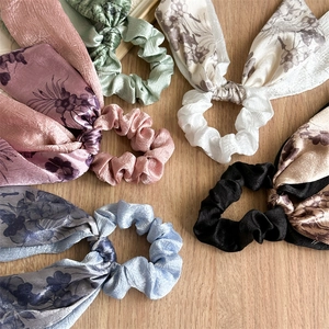 Detail of floral satin bow hair scrunchies in multiple pastel colors on wood background