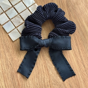 Detail of a black pleated satin scrunchie with bow and ruffles on light wood background