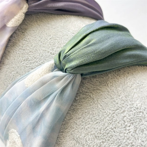 Close-up of twisted floral mesh headband showing elegant fabric texture and pleats