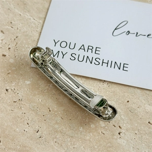 Close-up of a silver geometric metal spring hair clip on a minimalist stone texture