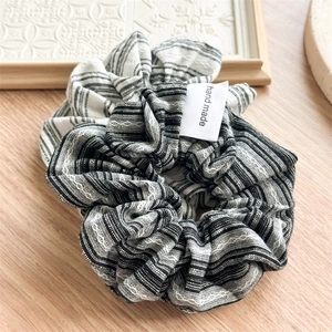 Classic black and white striped fabric scrunchie with handmade label on wooden surface