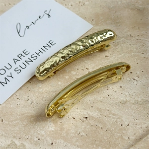 Detail view of gold geometric hair clip showing embossed texture and spring mechanism
