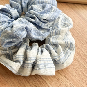 Close-up of blue and white striped fabric scrunchies on a textured wooden background