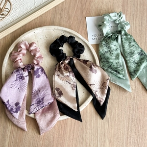 Three-piece floral satin hair scrunchies with long ribbons on a stone tray