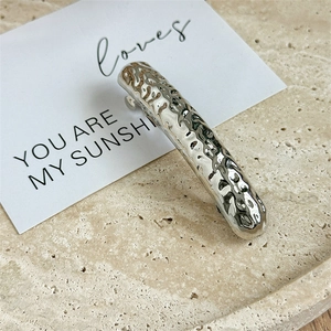 Macro detail of silver geometric hair clip showing hammered metal texture and wavy finish
