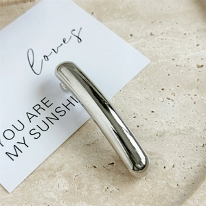 Detailed view of a silver minimalist metal spring hair clip on a beige textured stone tray