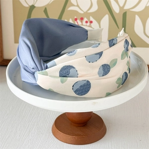 Detail of twisted knot headband with blue fabric and floral patterns on display stand