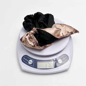 Close-up of a floral satin scrunchie with ribbons weighing 17g on a digital scale