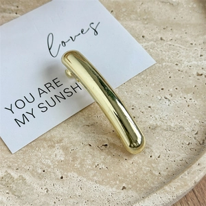 Macro detail of the polished golden curved hair clip on a minimalist stone tray display