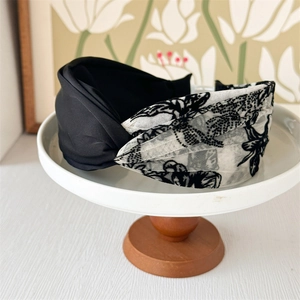 Detail of cross-knot headband with black satin and floral mesh texture on a stand