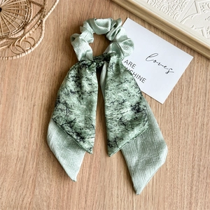 Detailed texture of sage green pleated satin hair scrunchie with marble pattern ribbon