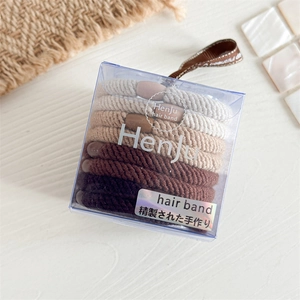 Detailansicht der erdigen Haargummis in einer transparenten Box auf einem Holztisch