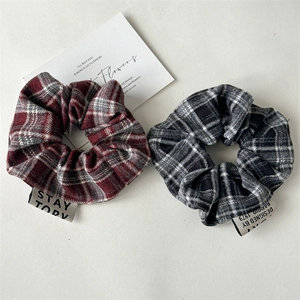 Detail view of two plaid scrunchies in red and grey with lettered fabric labels