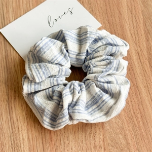 Detailed close-up of blue and white striped scrunchie with embroidered texture on wood