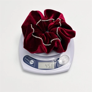 Macro shot of 45.8g deep red velvet hair scrunchie with rhinestones on a scale