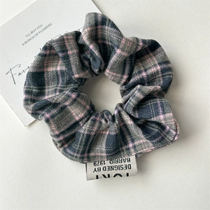 Detail view of plaid fabric scrunchie in grey and pink with a white woven design label