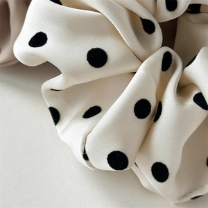 Detailed view of the smooth satin fabric texture and black polka dots on the scrunchie