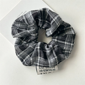 Detail of black and white plaid scrunchie with a white woven design tag on white surface