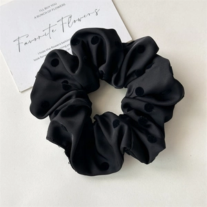 Close-up of black satin scrunchie with textured polka dots and pleated fabric design