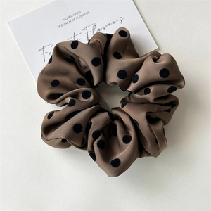 Close-up of brown satin scrunchie with black polka dots and soft texture detail