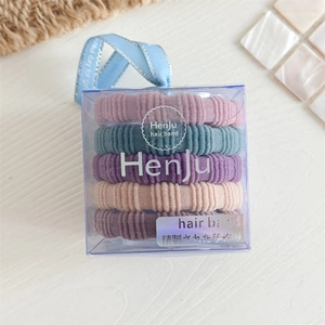Détail de cinq élastiques à cheveux rayés macaron dans une boîte avec ruban bleu