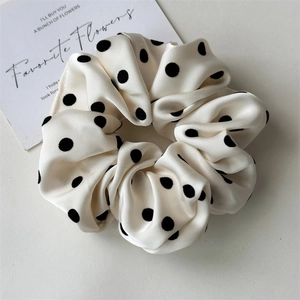 Detailed close-up of cream satin scrunchie with black polka dots on an elegant aesthetic background