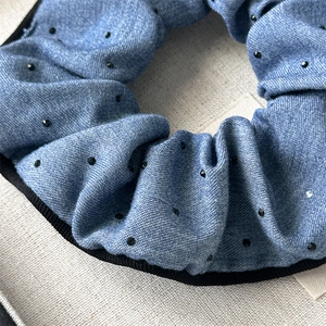 Close-up of blue denim scrunchie with small black rhinestones and black ribbon edge