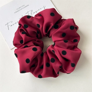 Detailed close-up of dark red satin scrunchie with elegant black polka dot patterns