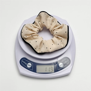 Detail view of a cream fabric hair scrunchie with black polka dots on a digital scale
