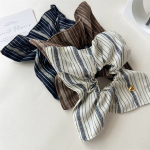 Close-up of three striped fabric scrunchies in navy, brown and beige with a heart charm