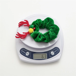 Detail shot of a green velvet Christmas scrunchie with red antlers weighing 6.3g on a scale