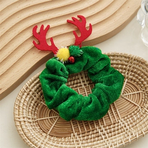 Close-up of green velvet Christmas hair scrunchie with red antlers and festive bells